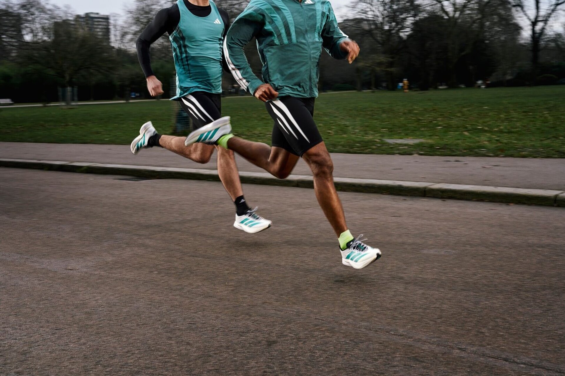 Zwei Läufer in schwarz-weiß-grünen adidas-Klamotten beim Joggen. Zu sehen sind Beine und Oberkörper.