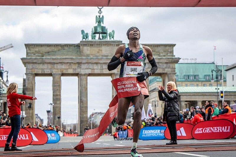 Sebastian Sawe läuft durchs Ziel des GENERALI BERLINER HALBMARATHON, im Hintergrund das Brandenburger Tor