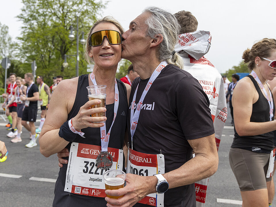 GENERALI BERLIN HALF MARATHON: Gesund im Ziel - ein Paar feiert den Zieleinlauf des GENERALI BERLINER HALBMARATHON 2024 mit einem Kuss. © SCC EVENTS // Jean-Marc Wiesner