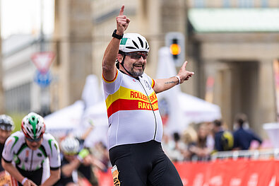 GENERALI BERLIN HALF MARATHON Inline Skating 2024: Skater joyfully reaches the finish line and raises his hands and index fingers © SCC EVENTS / Jean-Marc Wiesner / jeanmw.com