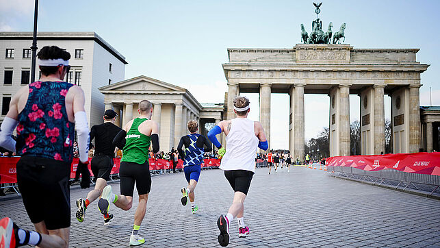  Fünf männliche Läufer laufen auf der Strecke richtung Brandenburger Tor 