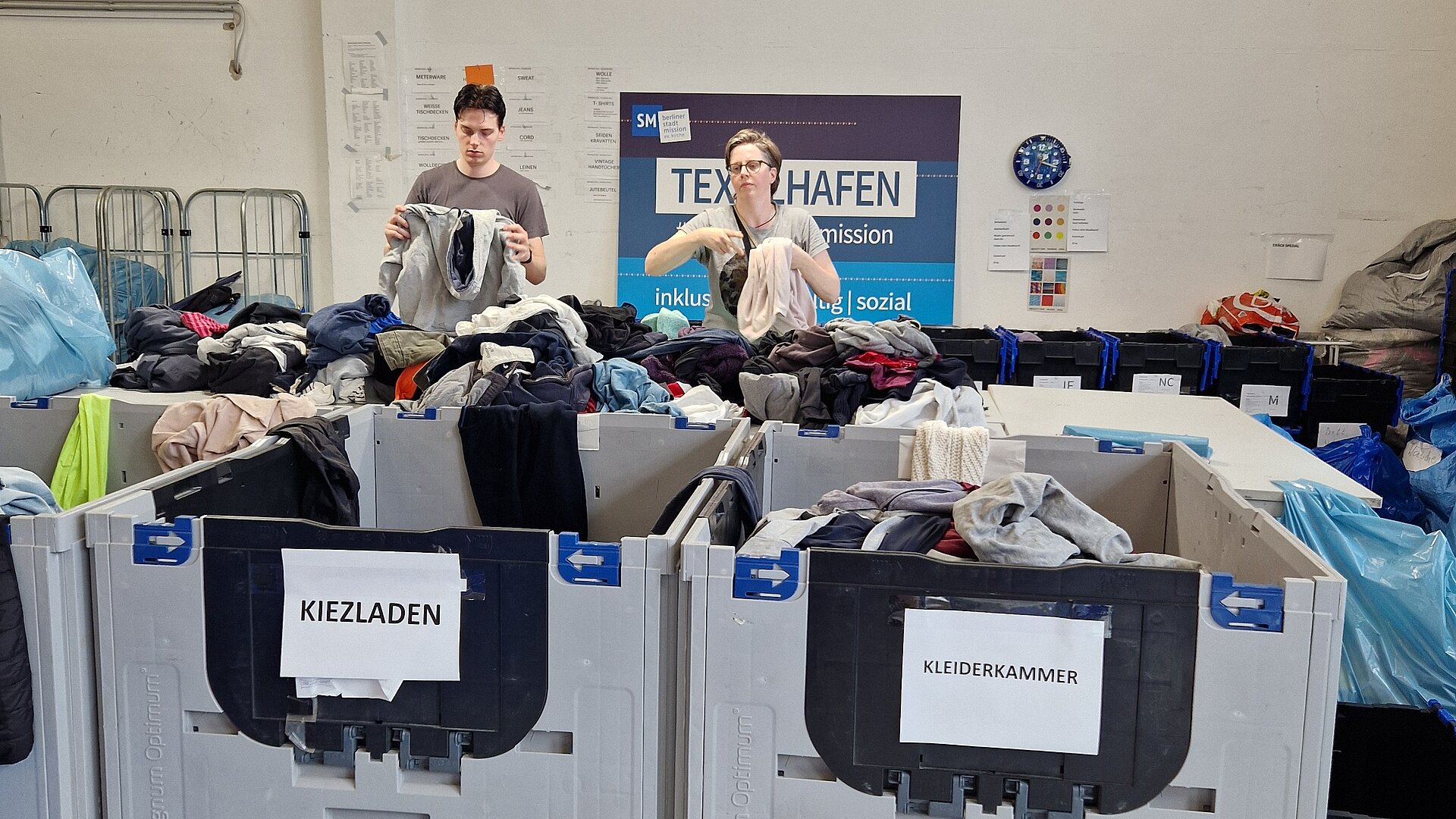 Zwei Mitarbeitende der Stadtmission sortieren Klamotten im Textilhafen.