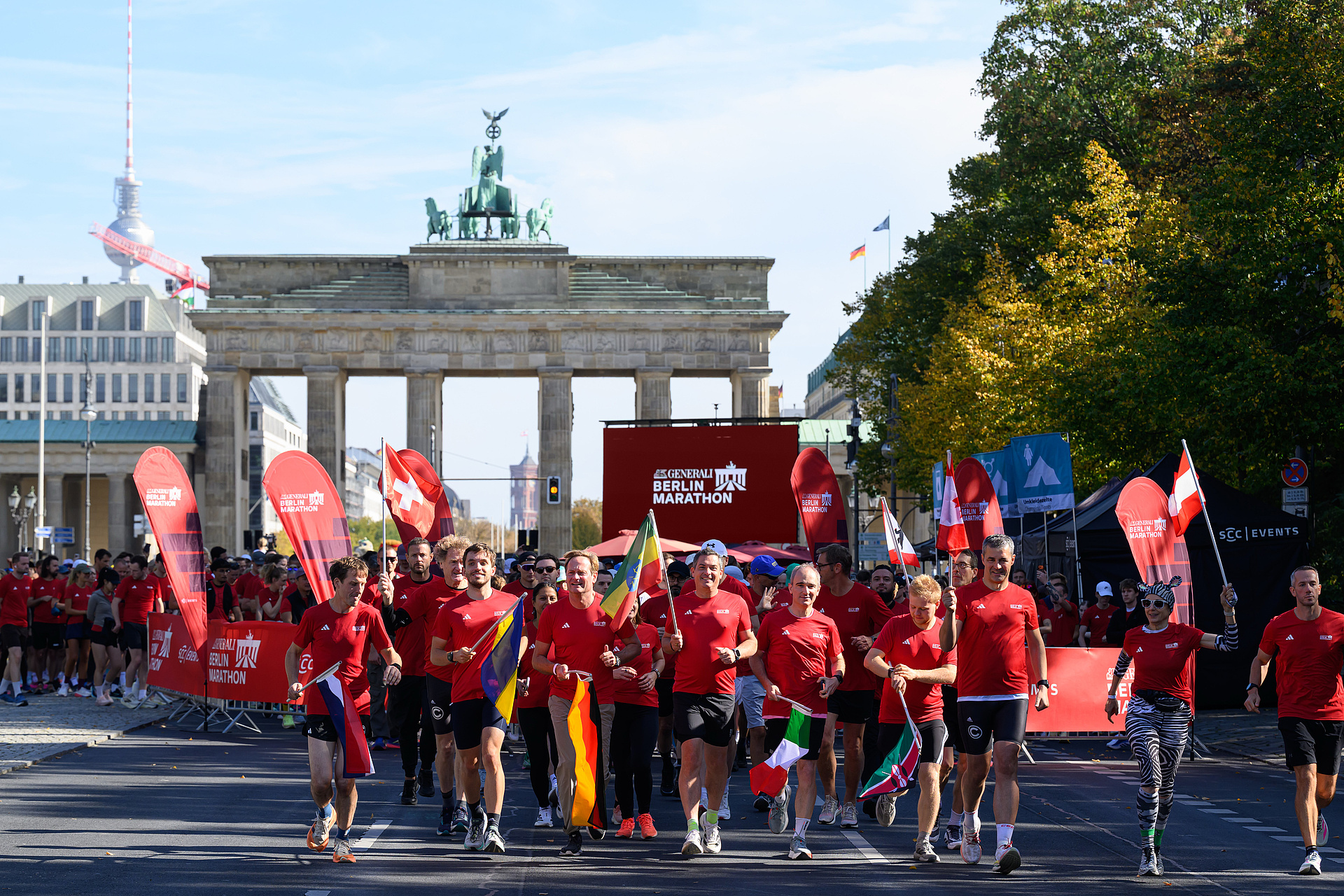 The start of the Registration Run, with participants all dressed in red and carrying various flags in front of the Brandenburg Gate.