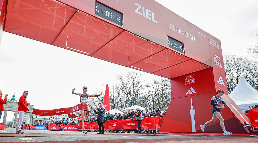 GENERALI Berliner Halbmarathon 2023: Die erste Frau läuft durch das Zieltor und reißt die Hände nach oben 