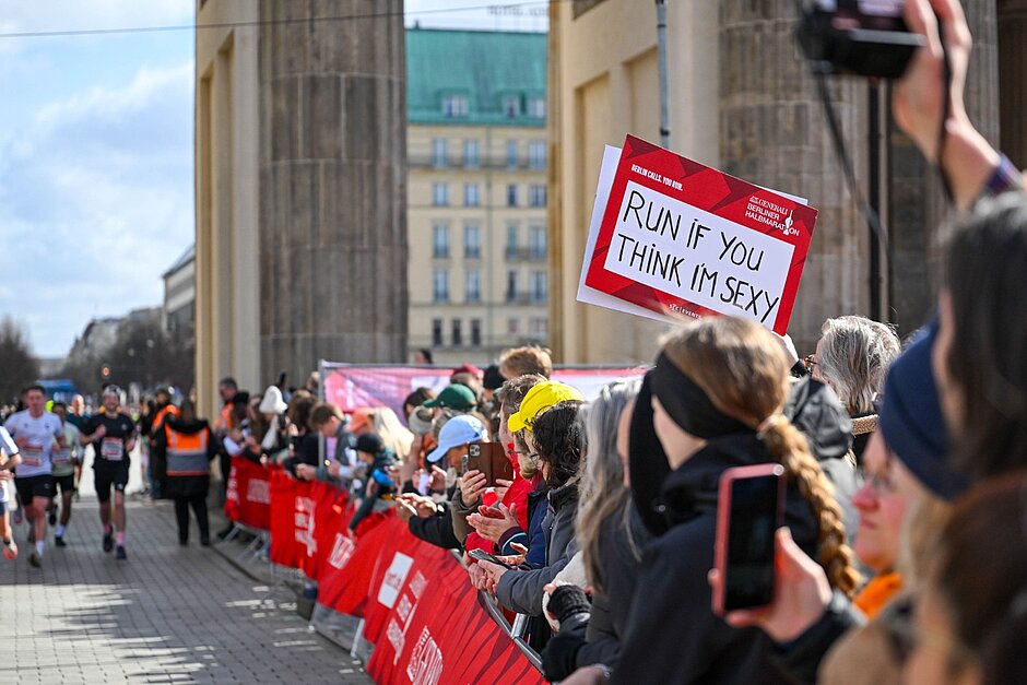 Spectators just behind the Brandenburg Gate. Someone is holding up a sign that reads ‘RUN IF YOU THINK I'M SEXY’.