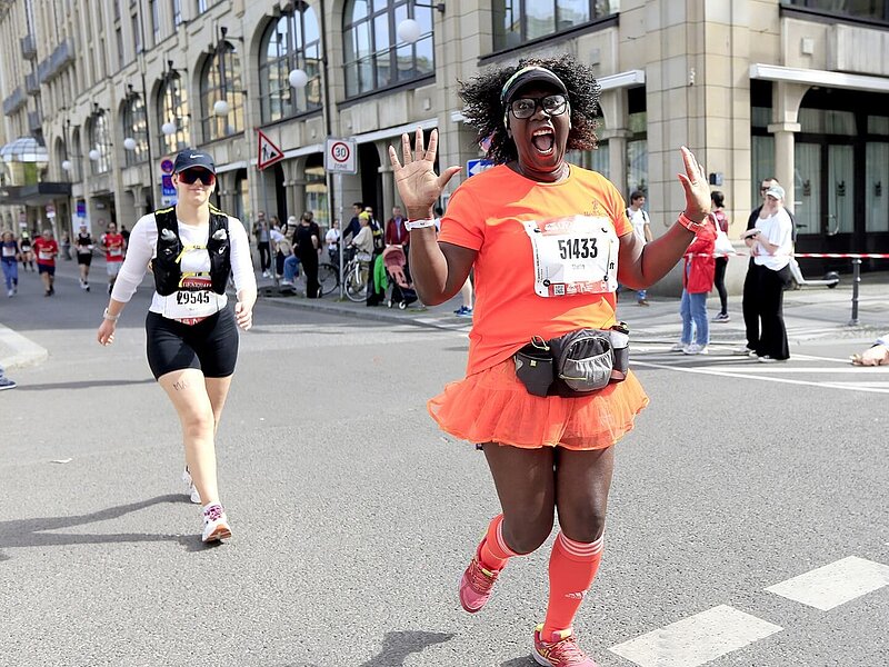 Lachende Läuferin mit Trinkgürtel, der Flasche und weitere Gegenstände enthält. Dahinter: Läuferin mit Trinkweste.