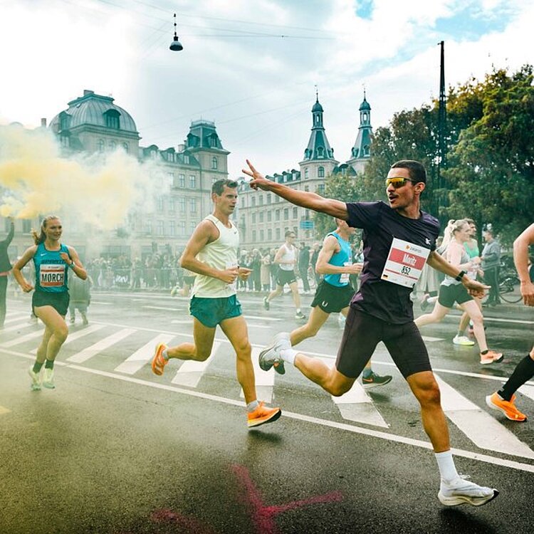 A dynamic close-up of runners on the track, one of whom is making the victory sign.