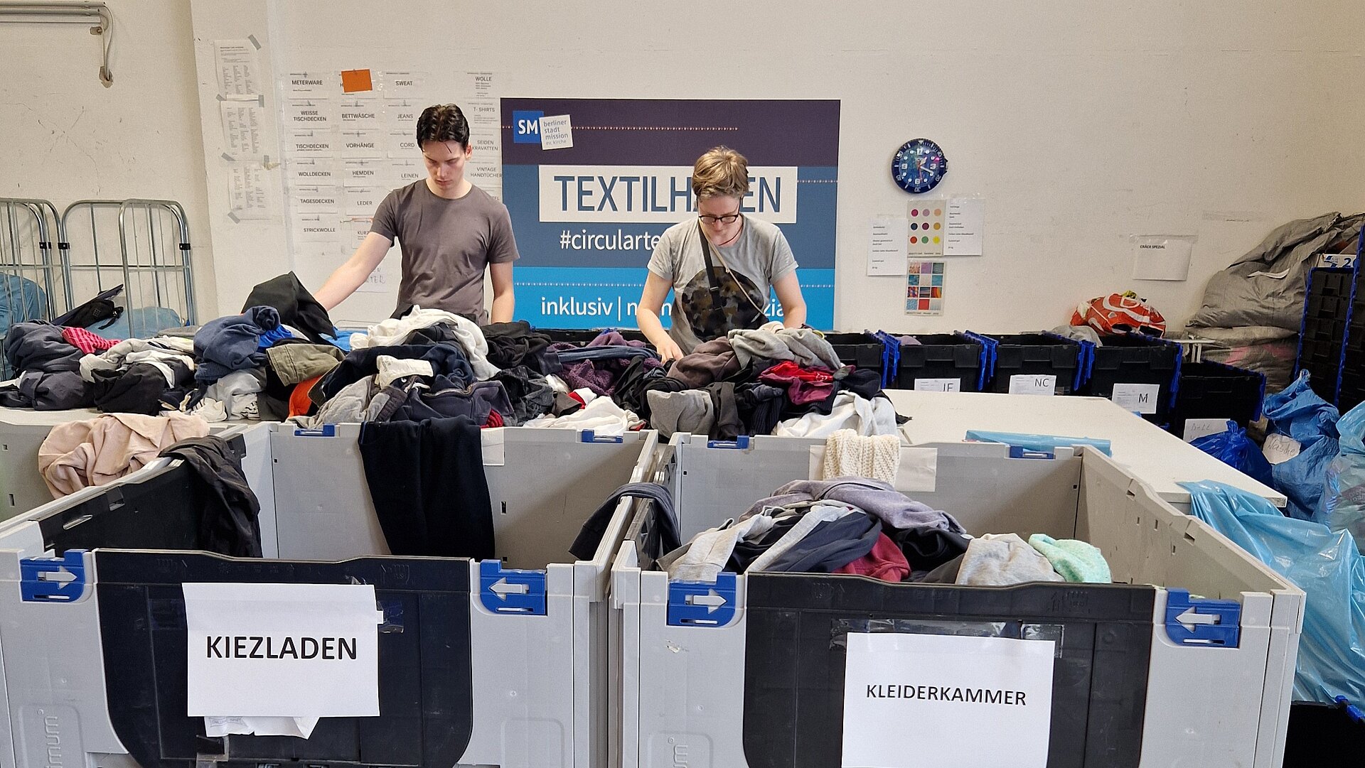 Lagerhaus, zwei Mitarbeiter sortieren gespendete Kleidung