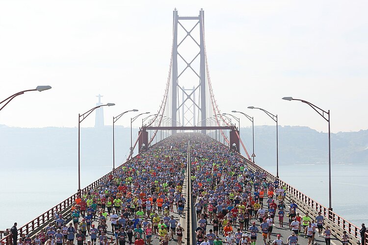 A striking aerial view of the runners at the start of the Lisbon Half Marathon on the famous “Ponte 25 de Abril” bridge.