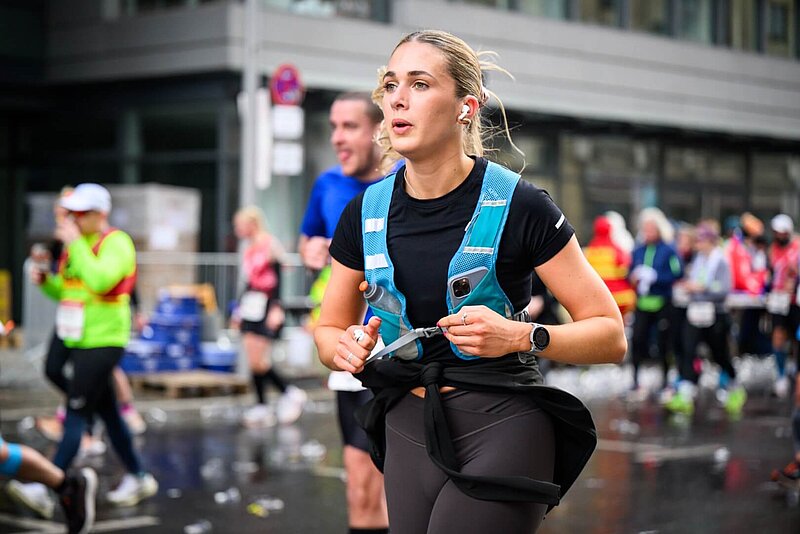 Fokussierte Läuferin mit Trinkweste, in der auch ein Smartphone steckt.