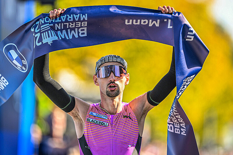 Hendrik Pfeiffer hält Zielband des BMW BERLIN-MARATHON 2025 triumphierend über dem Kopf.