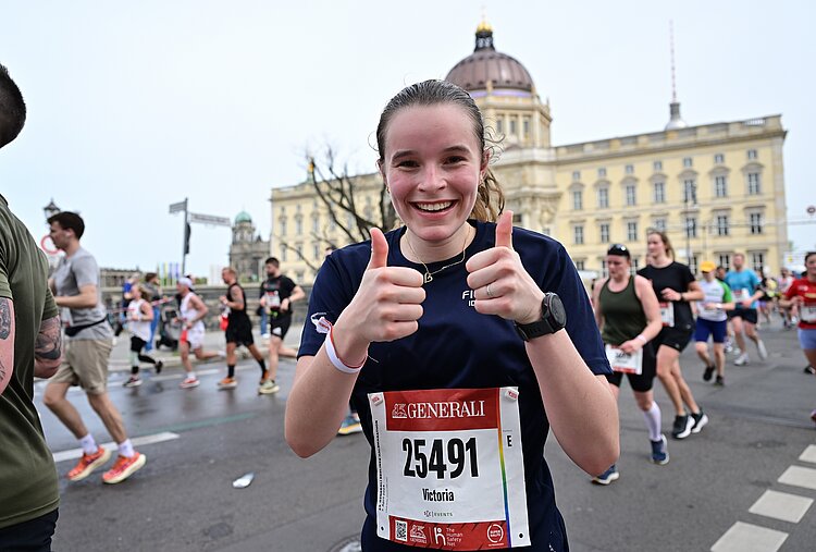 GENERALI BERLIN HALF MARATHON: Runner smiles at the camera and gives two thumbs up, Berlin Palace in the background © SCC EVENTS / Petko Beier