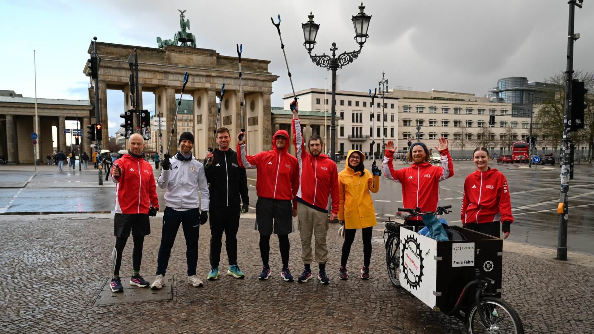 Teilnehmende halten ihre Müllgreifer für ein Gruppenbild vor Brandenburger Tor in die Luft. Rechts steht das Lastenrad.